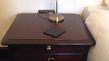 Une table de chevet en bois, avec une lampe, deux tiroirs et un petit objet noir posé sur le dessus.