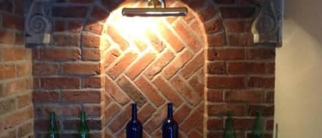 Una chimenea de ladrillo con un patrón de espiga, una barra de metal encima y dos botellas sobre la repisa.