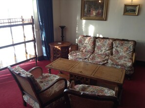 A traditional living room with a wooden coffee table, floral upholstered sofa, and wicker chairs. - The Crown Hotel (Thetford)