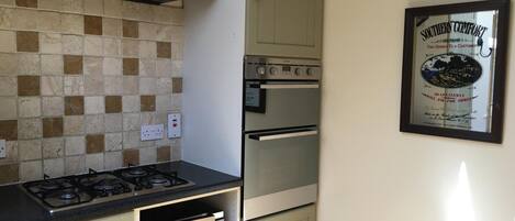 A kitchen with a gas stove, a built-in oven, and a wall-mounted microwave. There is a tiled backsplash and a framed sign on the wall.