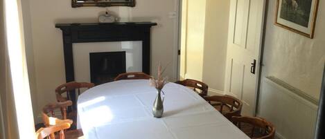 A dining room with a long table, wooden chairs, a fireplace, and a framed picture on the wall.