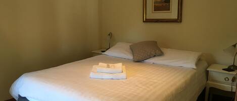 A neatly made bed with white linens, a pillow, and a folded towel on the bed. There is a framed picture on the wall above the bed.