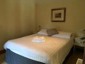 A neatly made bed with white linens, a pillow, and a folded towel on the bed. There is a framed picture on the wall above the bed. - The Crown Hotel (Thetford)