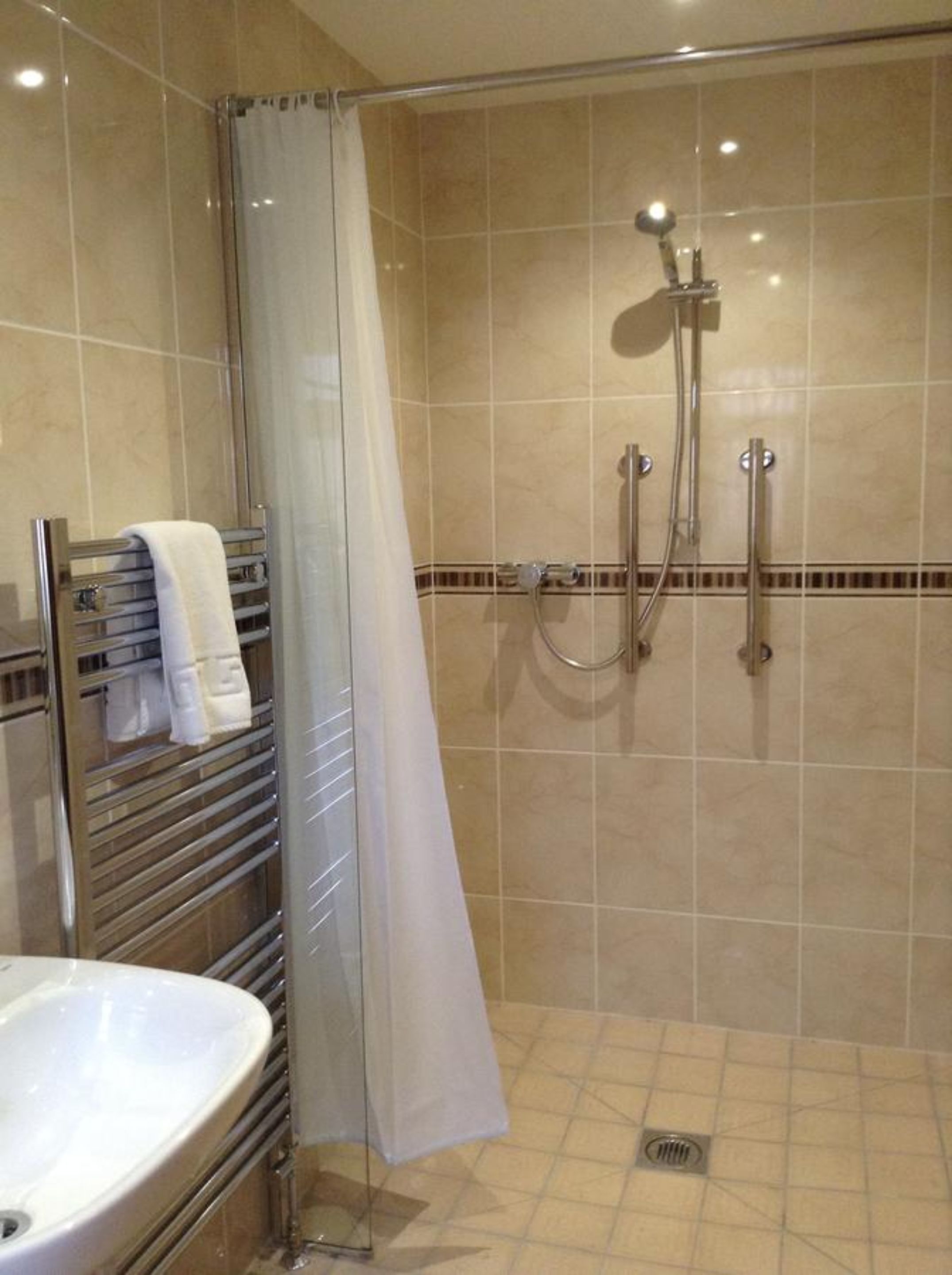 A shower with a glass door, a towel rack with towels, and a sink.
