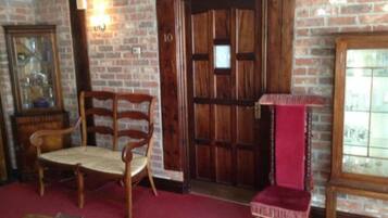 A room with a brick wall, a wooden door, a wooden chair, a red velvet chair, and a small table with a glass top.