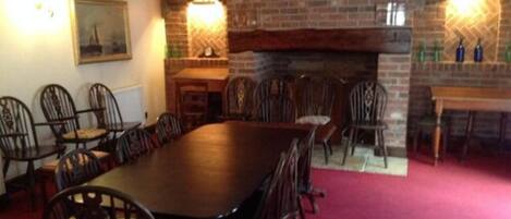 A dining area with a long wooden table and multiple chairs, a brick fireplace, and a painting on the wall.