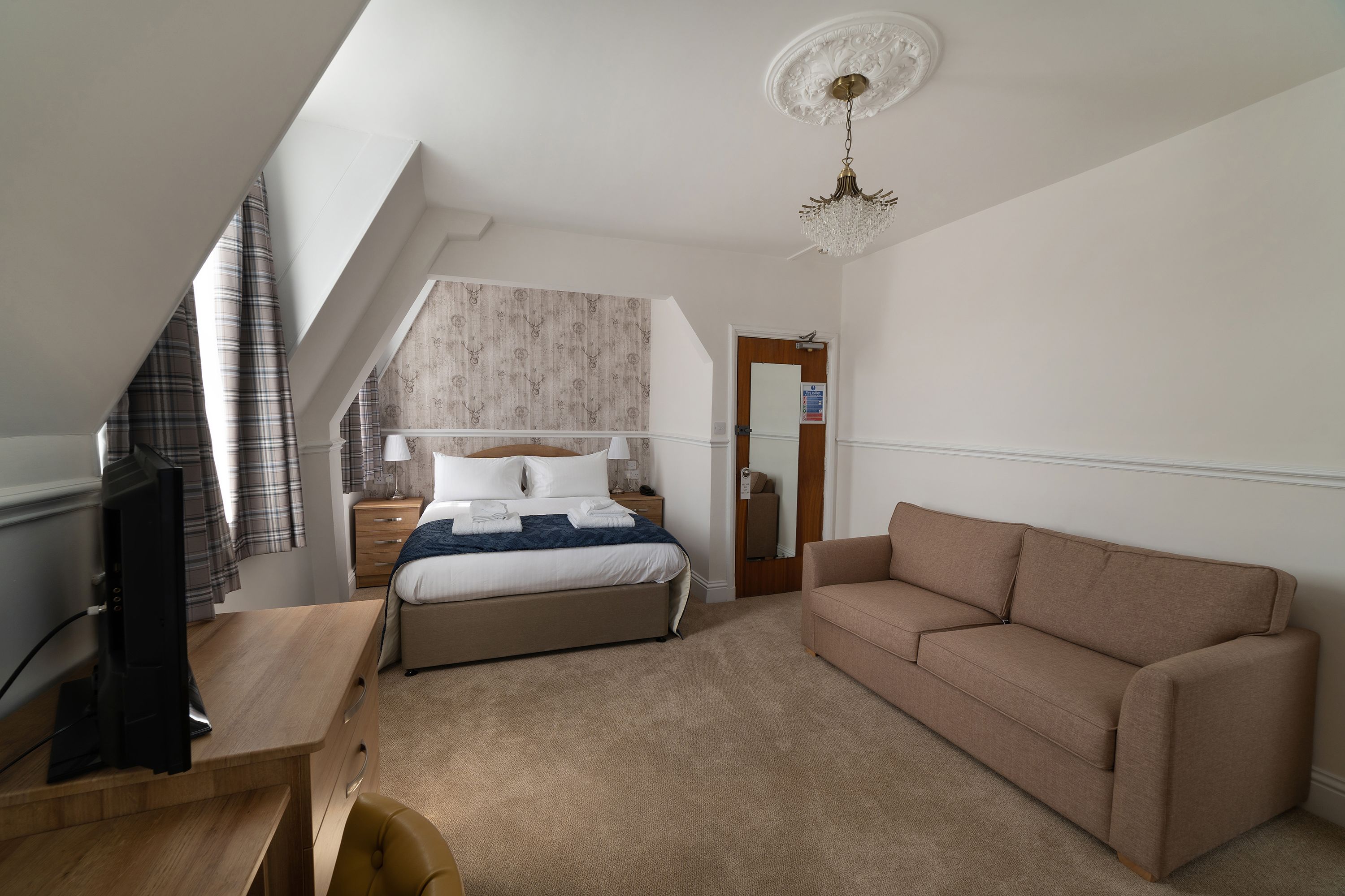 A bedroom with a bed, a desk, a sofa, and a television.