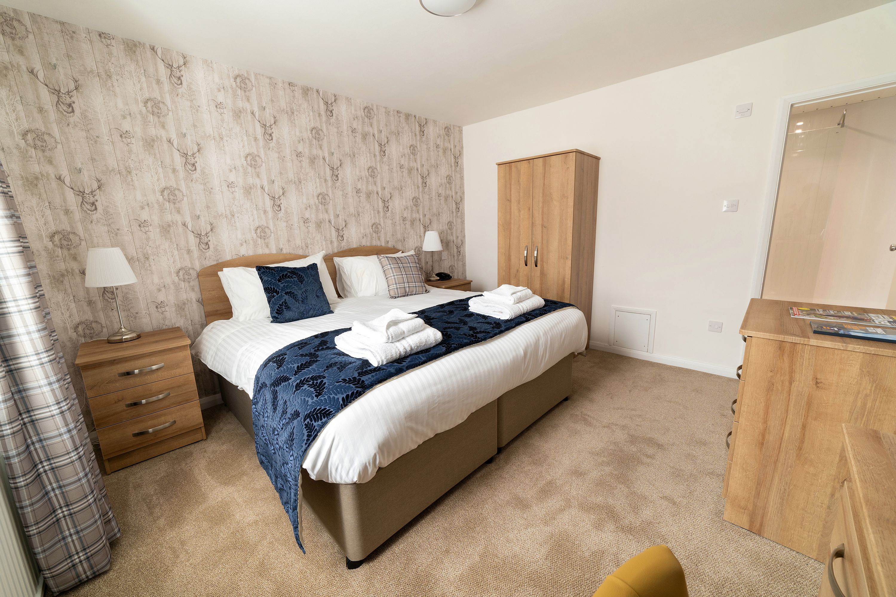 A bedroom with a bed, a wooden wardrobe, a nightstand, and a lamp.
