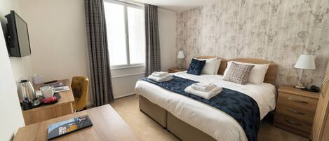 A hotel room with a bed, bedside tables, a desk, a chair, and a window with curtains.