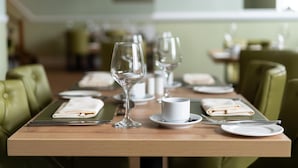 A dining table set with plates, glasses, and cutlery, with green upholstered chairs. - The Lakeland Kendal Hotel, Sure Hotel Collection by BW (Kendal)