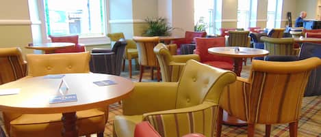 Un vestíbulo de hotel con varias zonas de estar, incluyendo mesas redondas y sillas con cojín.