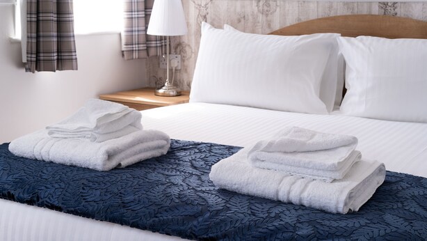A neatly made bed with white linens, a dark blue patterned throw blanket, and folded towels on the bed. - The Lakeland Kendal Hotel, Sure Hotel Collection by BW (Kendal)