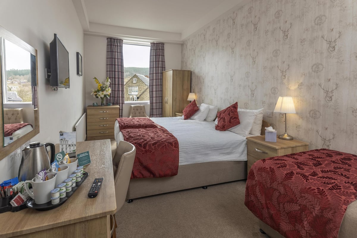A hotel room with a bed, bedside tables, a desk with coffee and tea, a mirror, and a window with curtains.