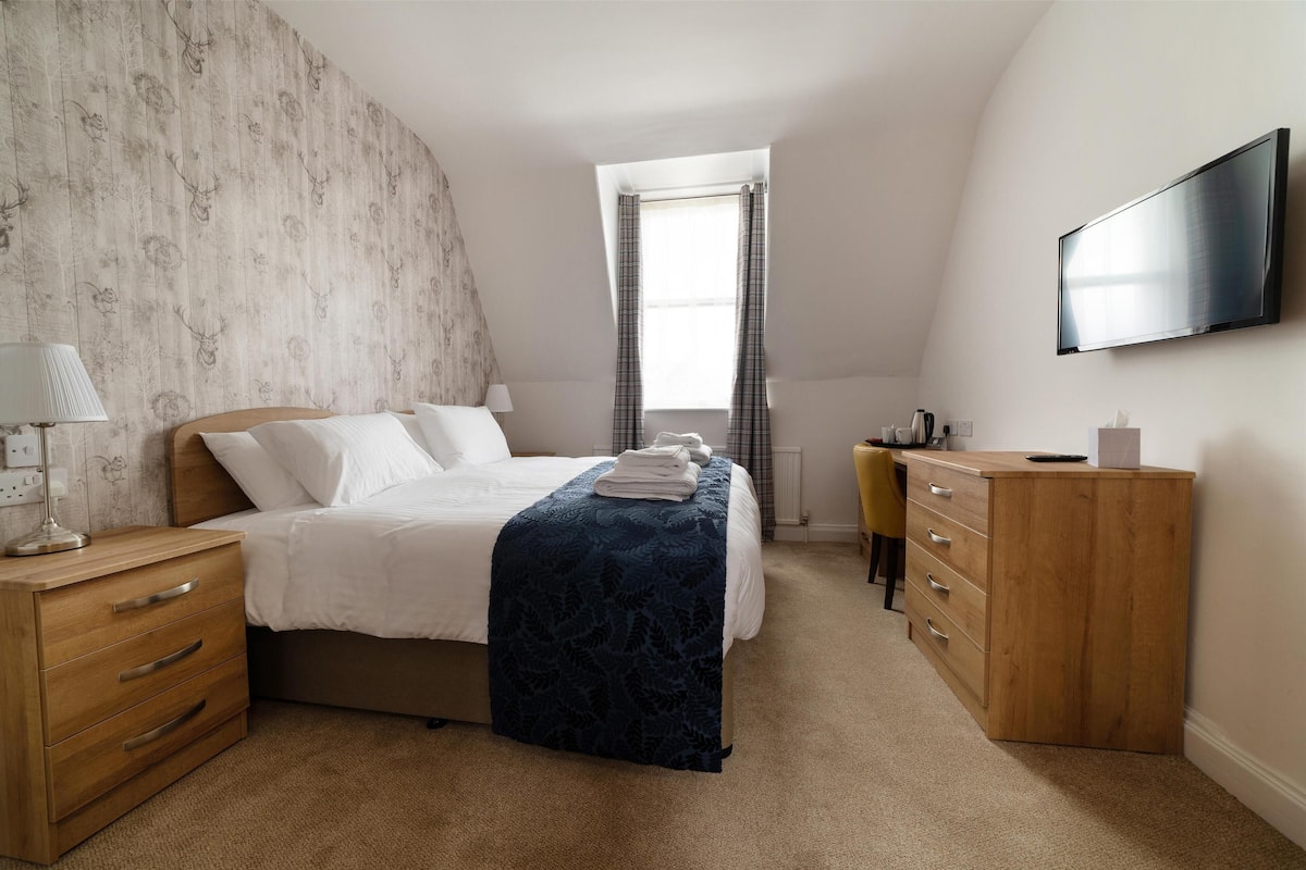 A bedroom with a bed, bedside tables, a desk, a chair, a wardrobe, and a television.