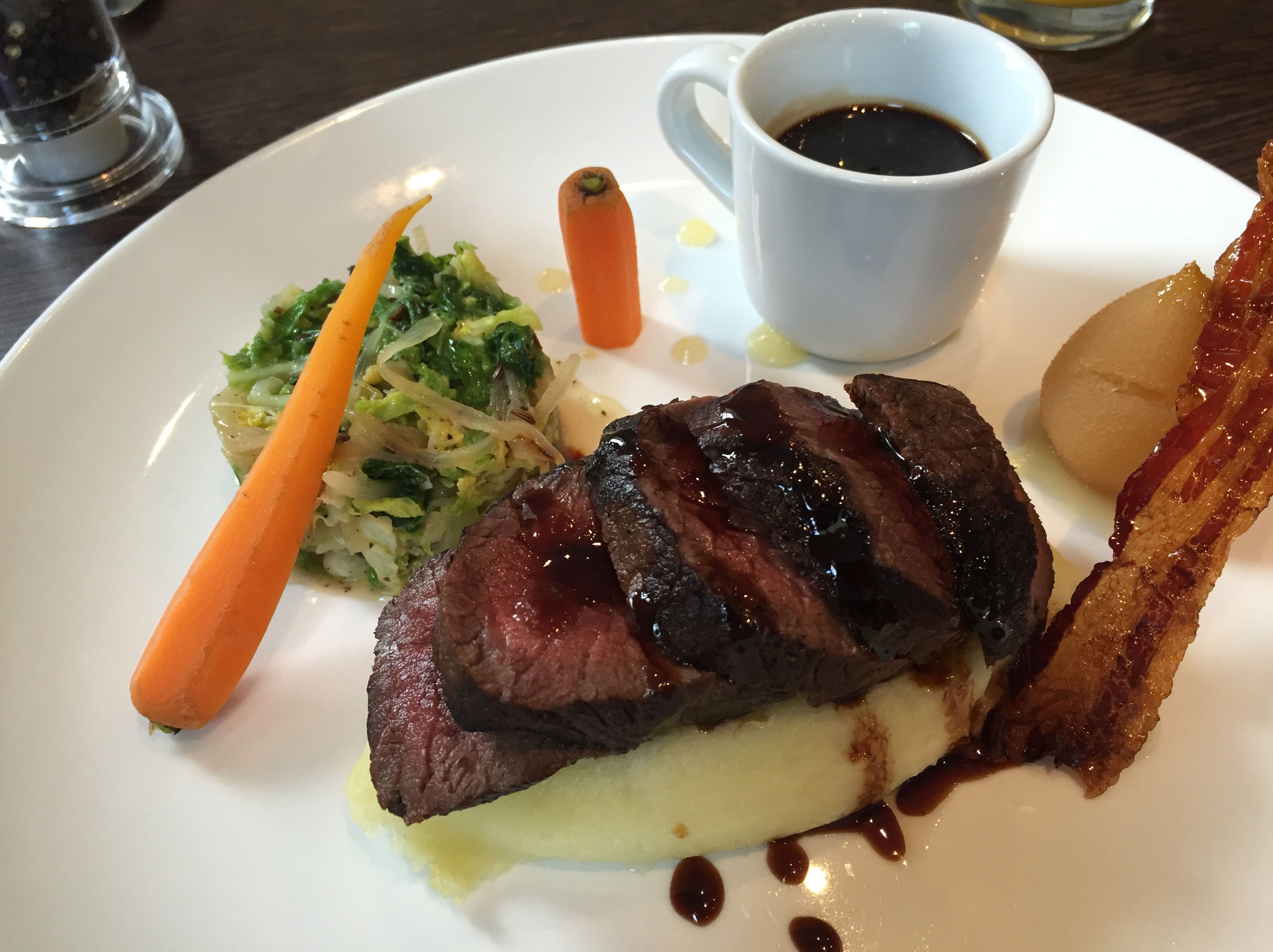Prato com bife, bacon, cenoura e uma xícara de café.