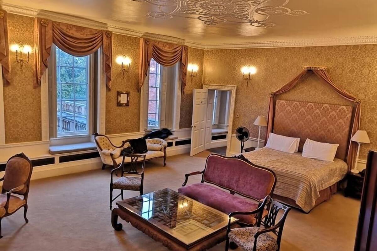 A spacious bedroom with a four-poster bed, a glass-top coffee table, two armchairs, and a chaise lounge.