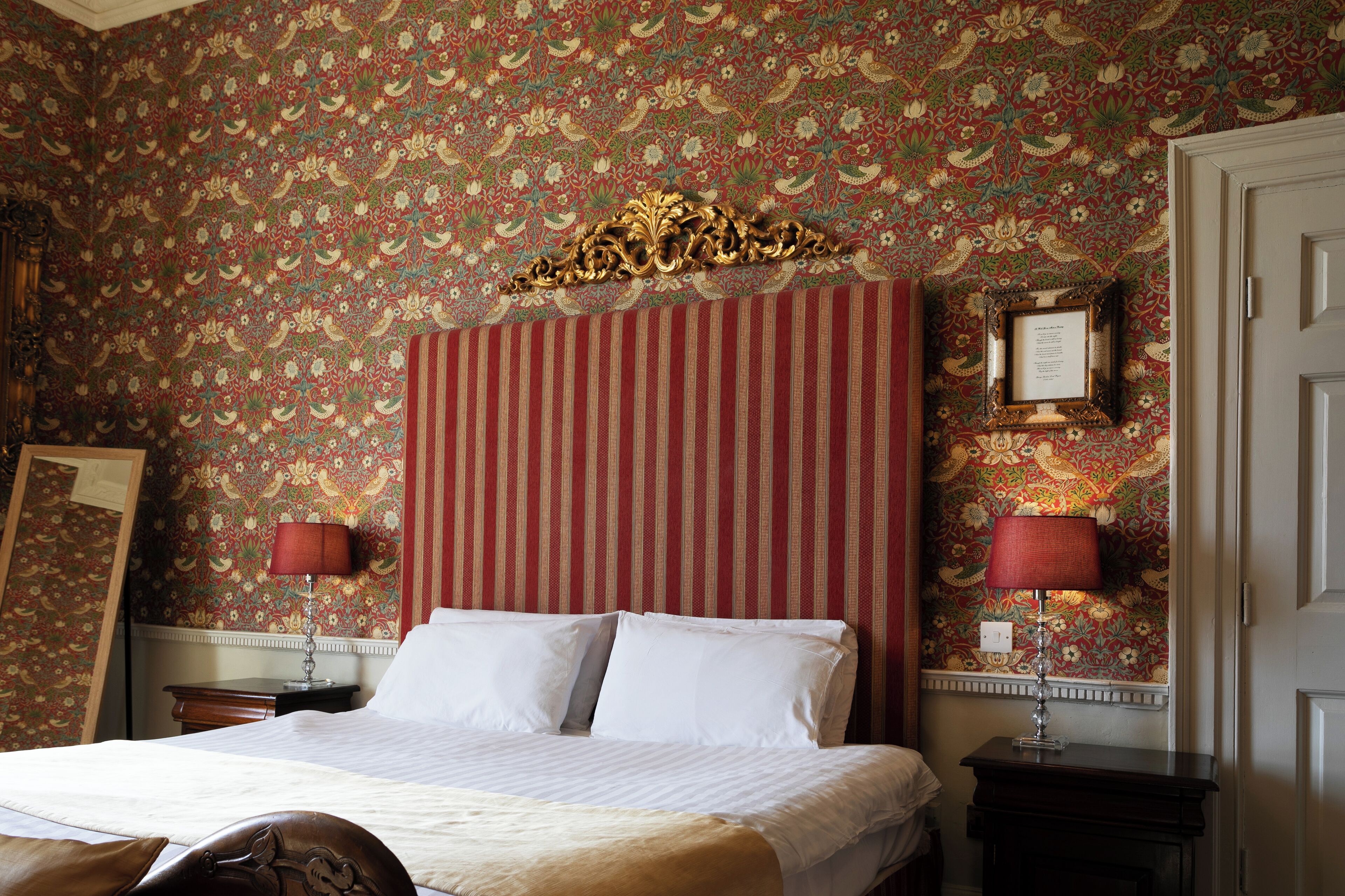 Une chambre d’hôtel avec un grand lit, une tête de lit à rayures, un papier peint à motifs floraux et deux lampes de chevet.