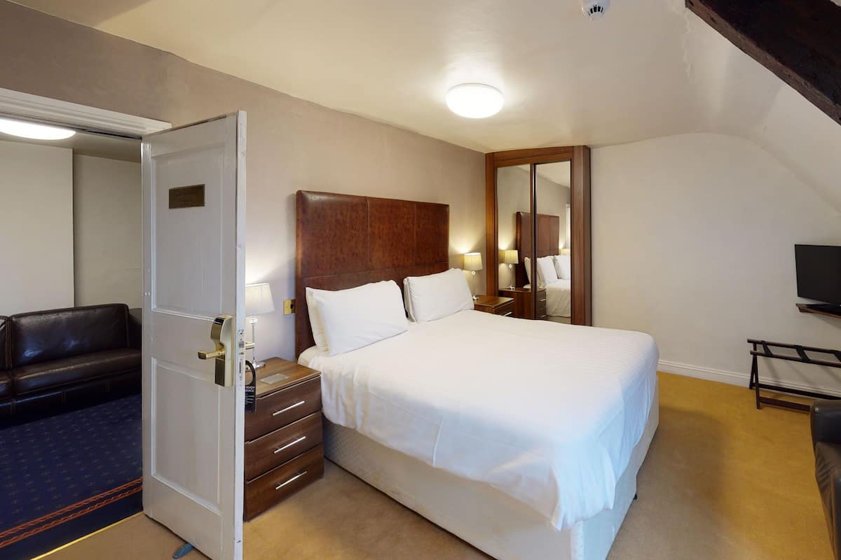 A hotel room with a bed, bedside tables, a mirror, a TV, and a ceiling fan.