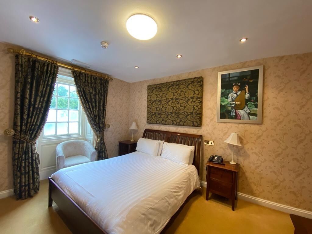 A hotel room with a large bed, a chair, a nightstand with a lamp, and a painting on the wall.