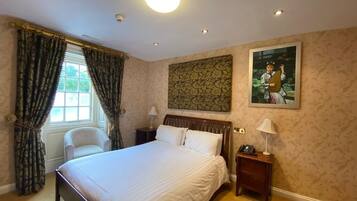 A hotel room with a large bed, a chair, a nightstand with a lamp, and a painting on the wall.