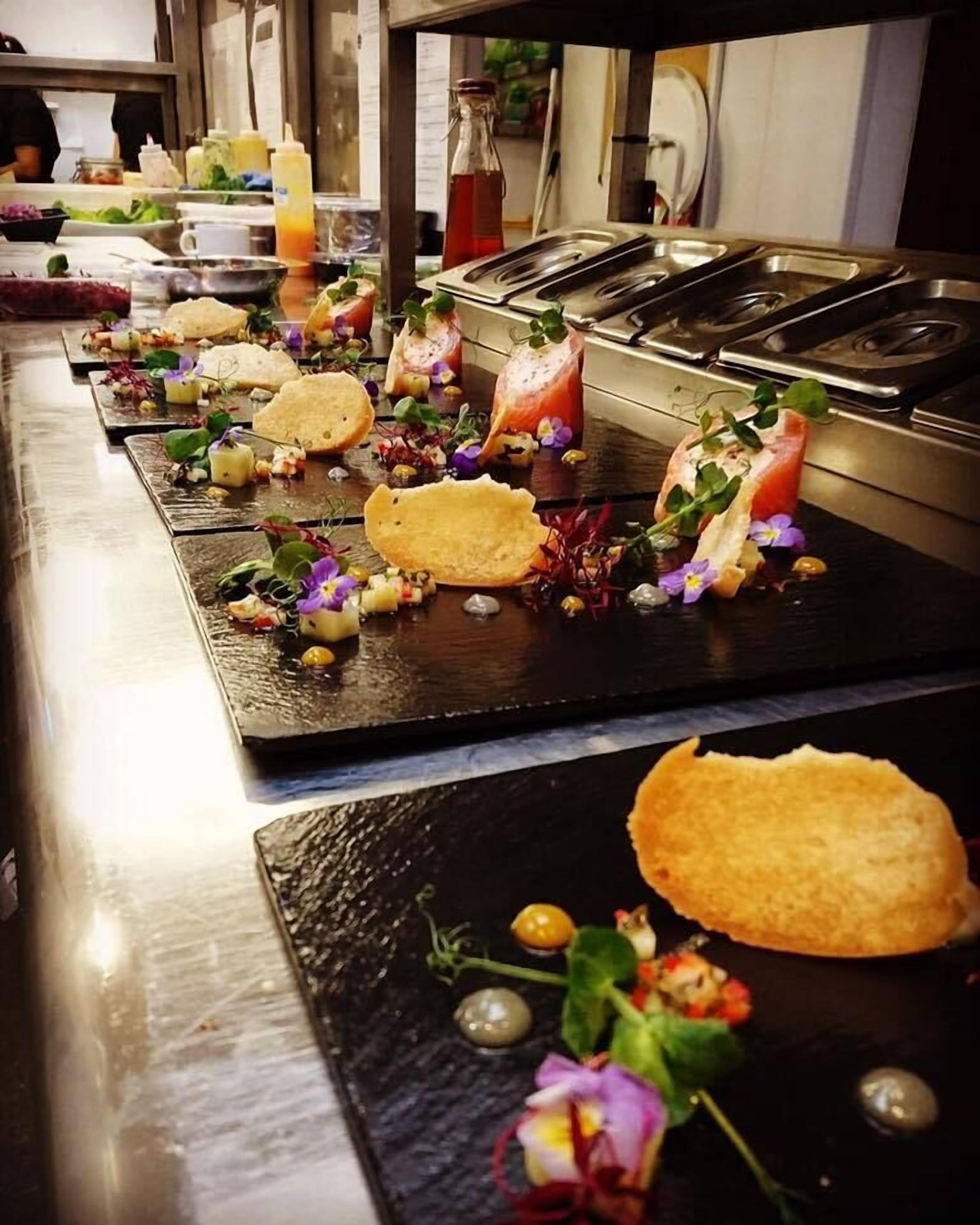 Una fila de platos elegantemente presentados, con diferentes guarniciones y salsas, dispuestos sobre una mesa larga en un restaurante.