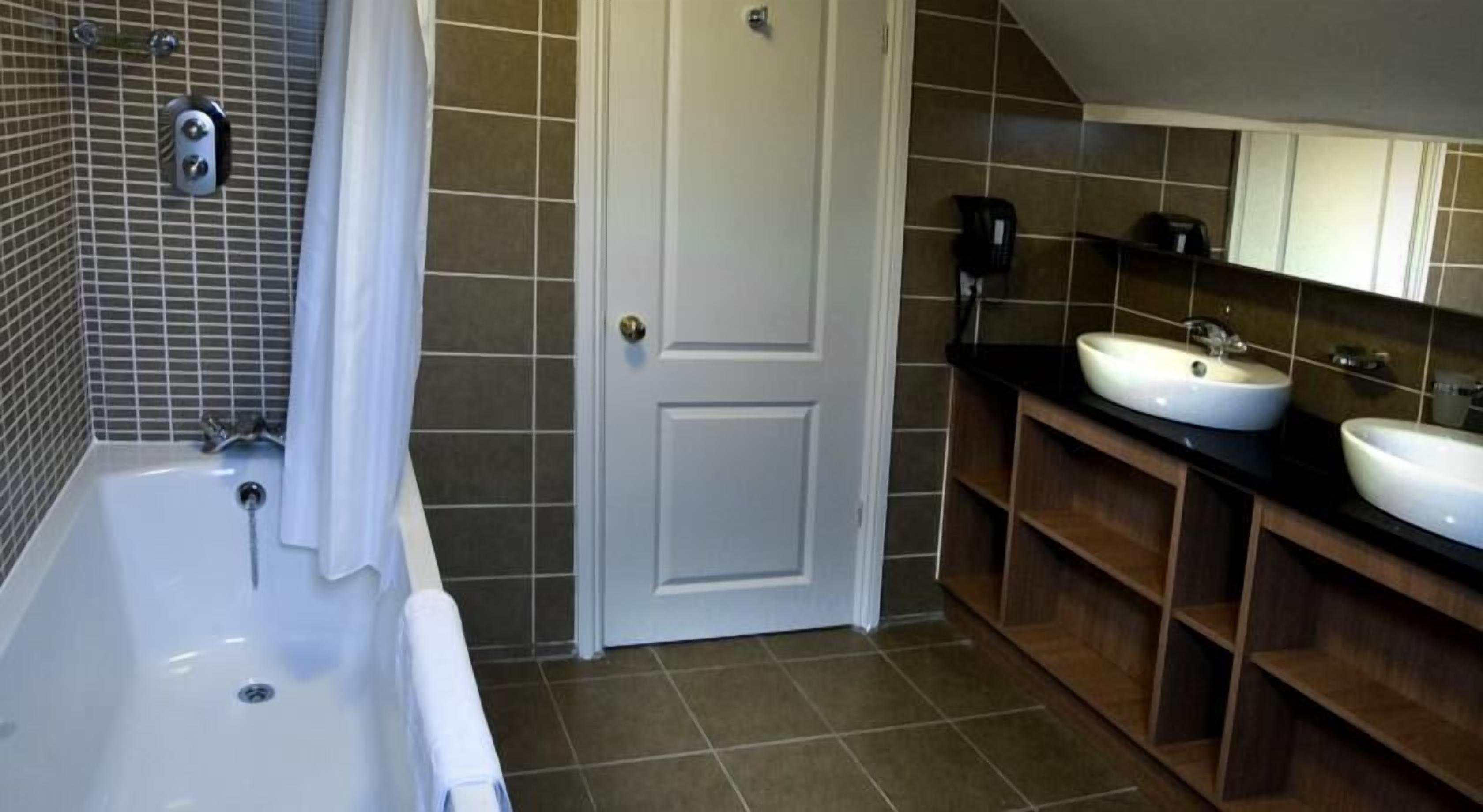 A bathroom with a bathtub, two sinks, a door, and tiled walls.