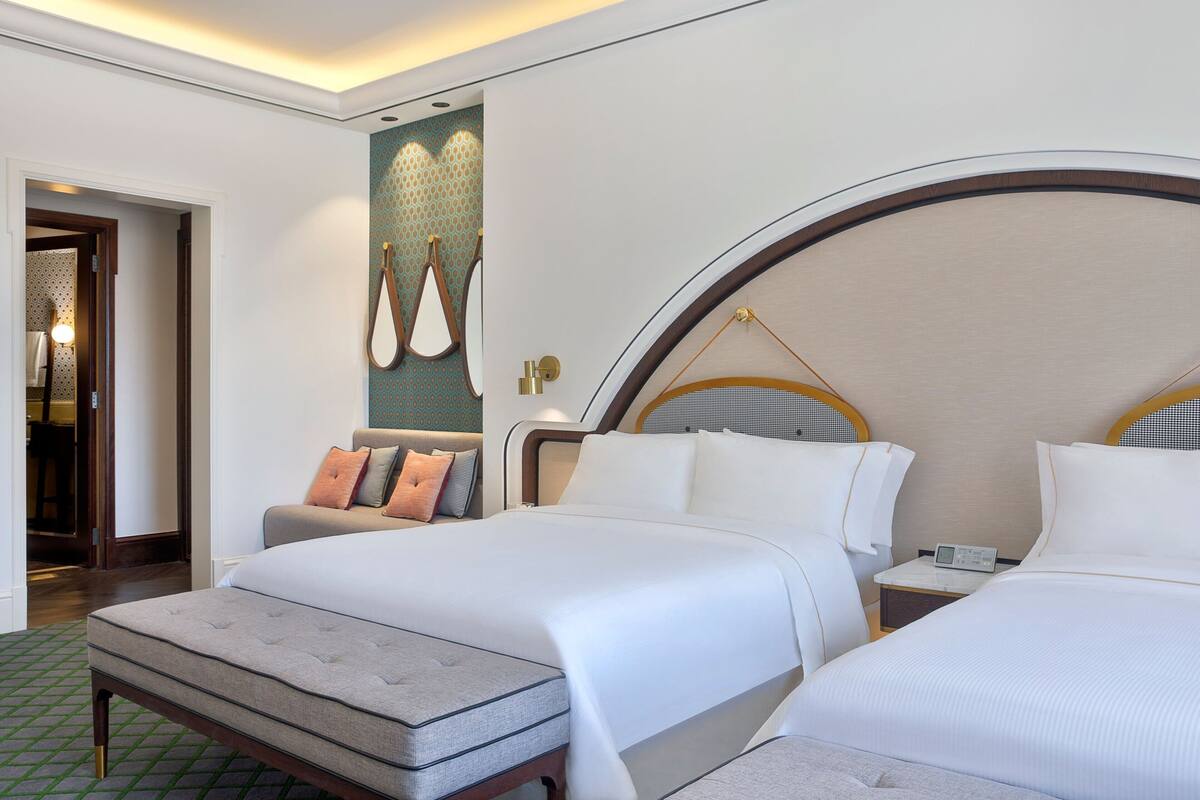 Une chambre d’hôtel avec deux lits, un canapé, une grande œuvre d’art murale et une table de chevet avec une lampe.
