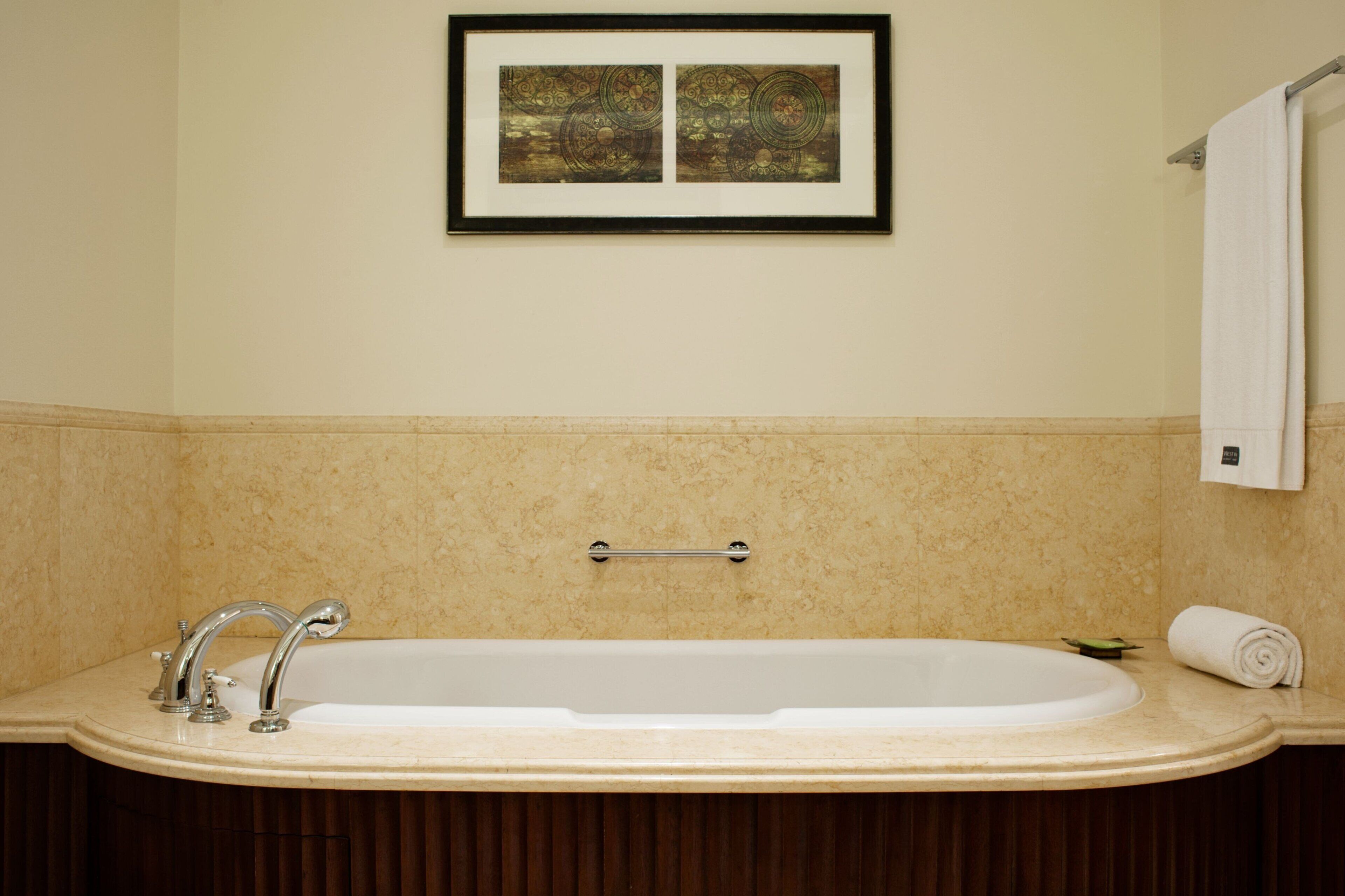A bathroom with a large bathtub, a framed artwork above the tub, and a towel rack with a towel.