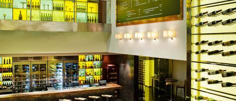 Zona de bar con varias estanterías llenas de botellas, un tablero de menú y taburetes.