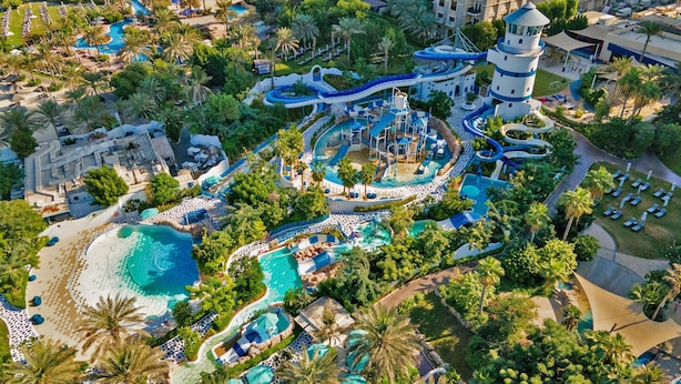 Vista aérea de un complejo turístico con varias piscinas, parque acuático y una estructura tipo torre.