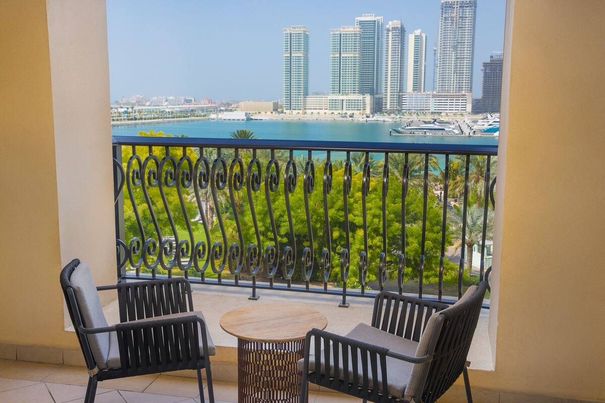 Un balcon avec deux chaises et une petite table, donnant sur une marina où sont amarrés des bateaux et sur le panorama de la ville.