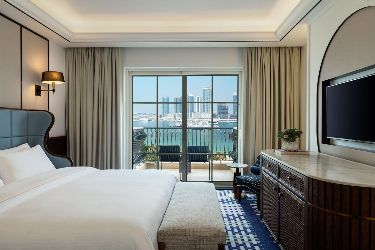 Une chambre d’hôtel avec un grand lit, une télévision, un balcon donnant sur la ville et un bureau avec une chaise.