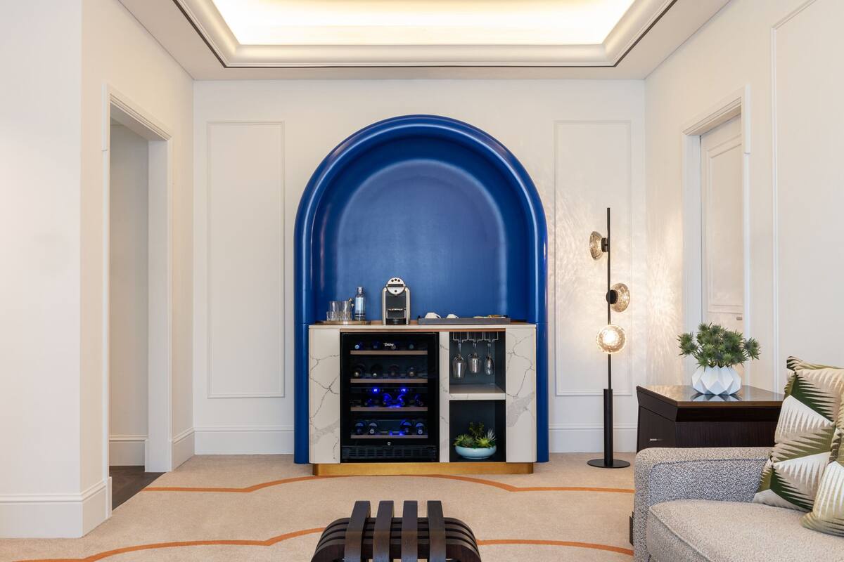 Un salon moderne avec une arche bleue, un réfrigérateur à vin, une lampe sur pied et un canapé agrémenté de coussins décoratifs.