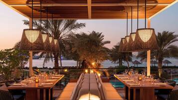 An outdoor dining area with a long table set for a meal, overlooking a pool and palm trees.