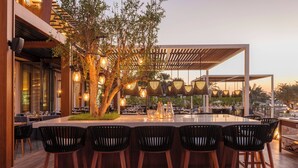 An outdoor dining area with a long table and black chairs, surrounded by trees and a pergola with hanging lights. - The Westin Dubai Mina Seyahi Beach Resort & Marina (Dubai)