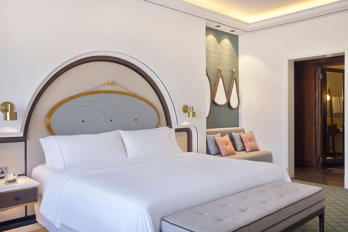 Une chambre d’hôtel moderne avec un grand lit, un grand miroir rond au-dessus du lit, une table de chevet avec une lampe et un porte-serviettes fixé au mur.