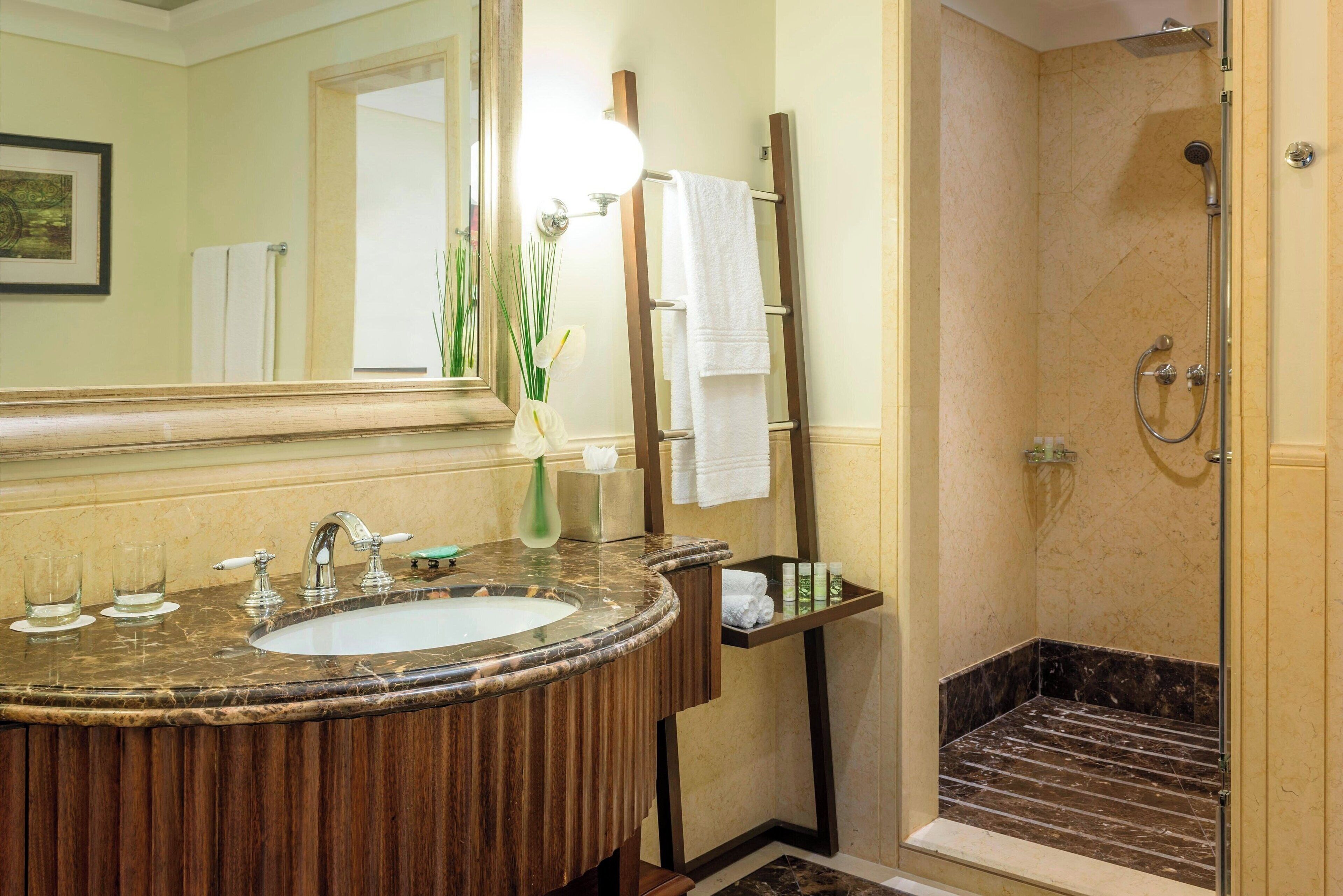 A bathroom with a marble sink, a mirror, a towel rack, and a shower area.