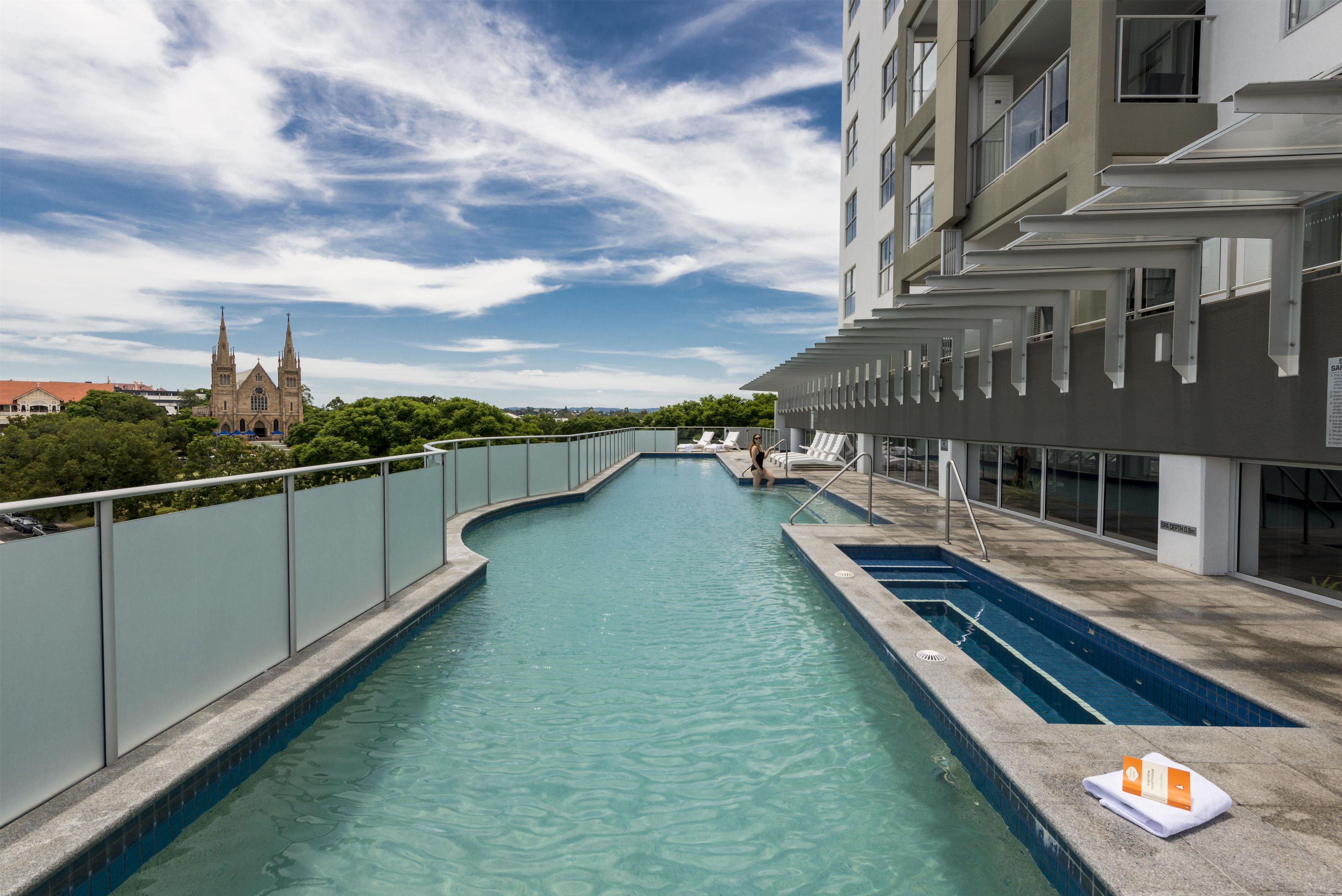 A swimming pool with a curved design, surrounded by a high fence, and a building with multiple balconies in the background.