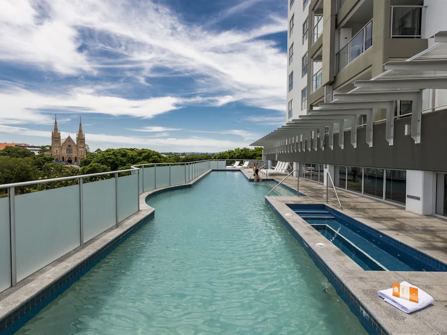 Una piscina con un design curvo, circondata da un recinto alto, e un edificio con diversi balconi sullo sfondo.