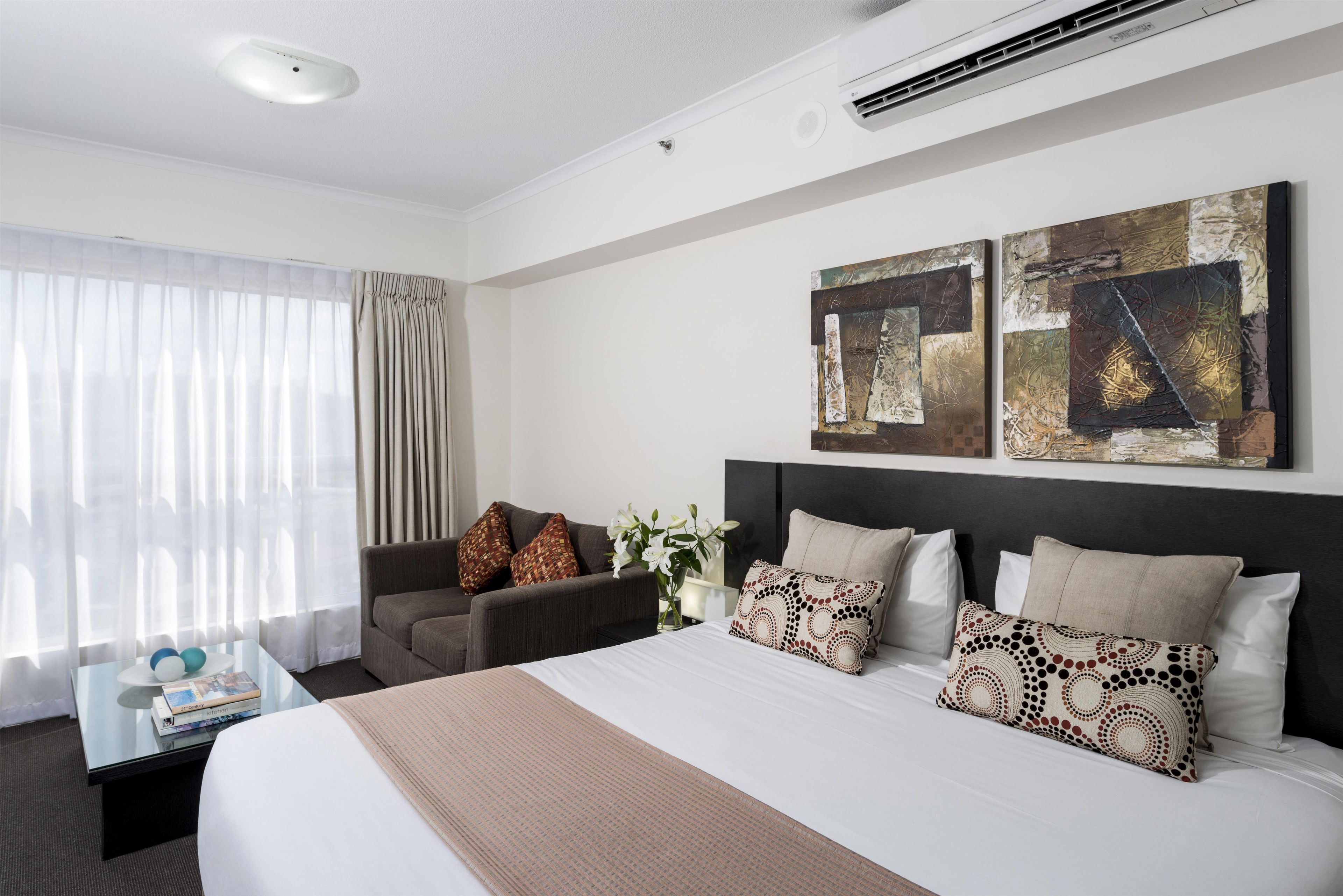 A hotel room with a large bed, a sofa, a coffee table, and two wall-mounted artworks.