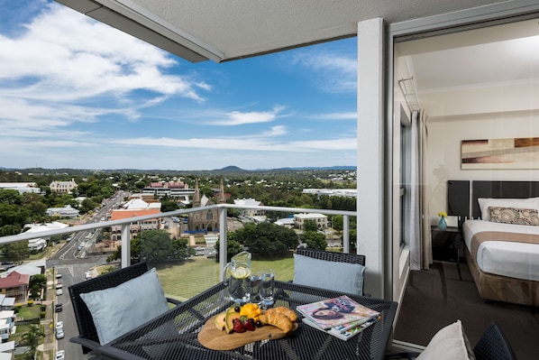 Ein Balkon mit Frühstückstisch, einem Bett und Blick auf die Stadt.