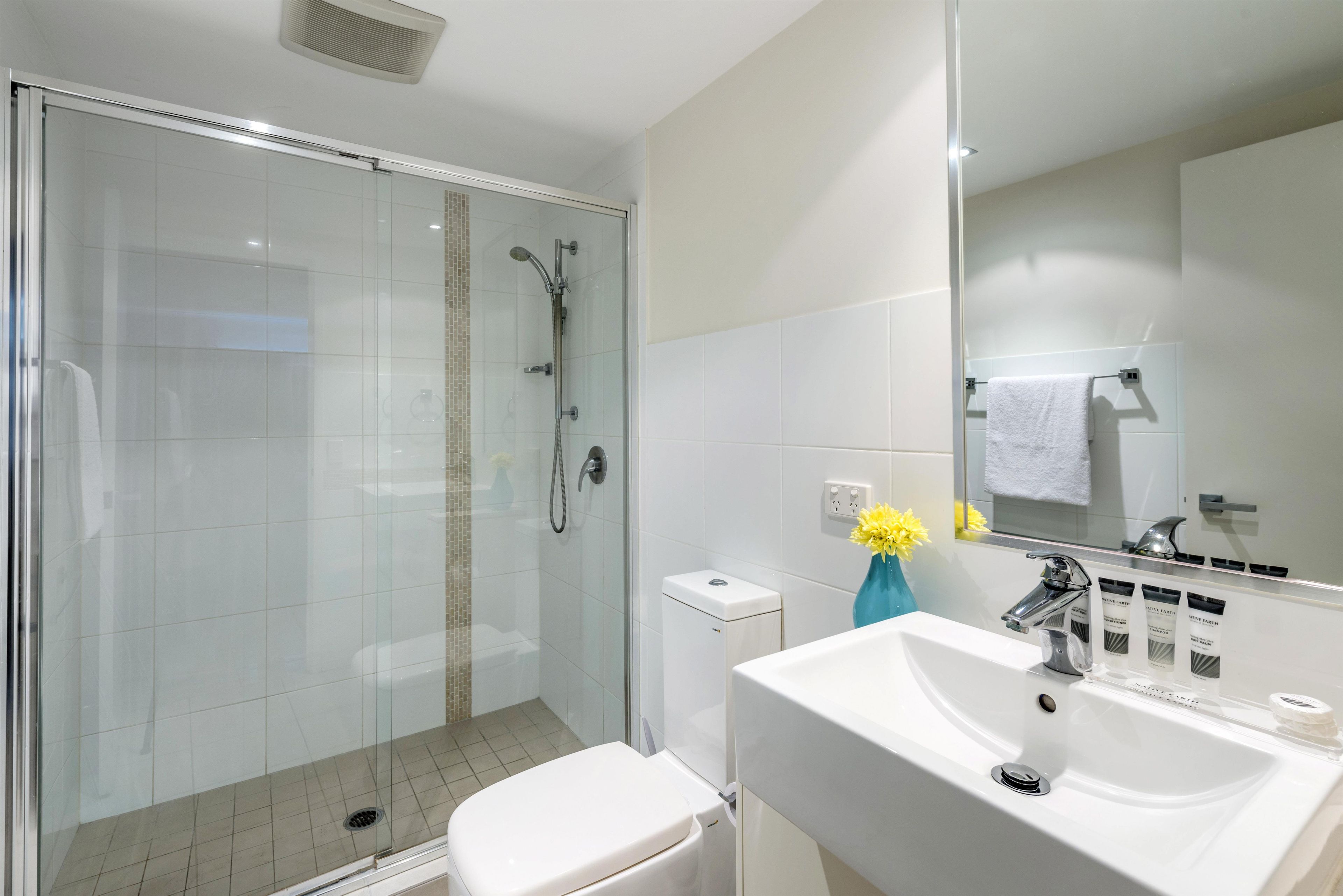 A modern bathroom with a glass-enclosed shower, a white toilet, and a sink with toiletries.