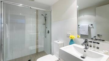 A modern bathroom with a glass-enclosed shower, a white toilet, and a sink with toiletries.