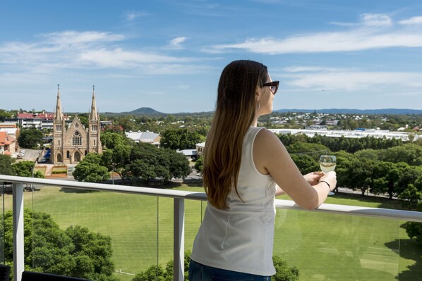A person on a balcony overlooking a church, grassy area, and residential buildings.