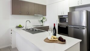 A modern kitchen with white countertops, stainless steel appliances, and a wooden cutting board with cheese and grapes.