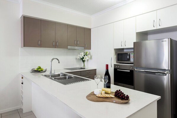 Una cocina moderna con encimeras blancas, electrodomésticos de acero inoxidable y una tabla de madera con queso y uvas.