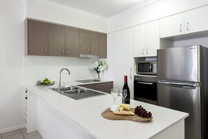 Una cocina moderna con encimeras blancas, electrodomésticos de acero inoxidable y una tabla de madera con queso y uvas.