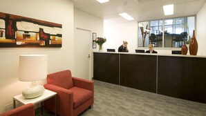 A reception area with a desk, chairs, a painting, and a window with a view.