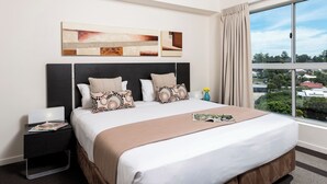 A hotel room with a large bed, a nightstand, a window with a view of the city, and artwork on the wall.