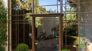 A hotel entrance with a large glass facade, a sign reading "The Kefalaris Suites," and potted plants in front.